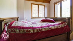 Ein Schlafzimmer mit einem Holzbett, einem Fenster mit Spitzenvorhängen und einer Holzbalkendecke.
