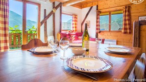 Mesa de madera dispuesta con platos, vasos y una botella de vino, con vistas panorámicas a la montaña a través de amplias ventanas.