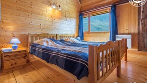 Un dormitorio de cabaña de madera con cama, mesita de noche, lámpara y ventana con cortinas.
