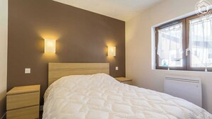 Un dormitorio con una cama grande, dos mesitas de noche, una ventana con cortinas y lámparas fijadas a la pared.