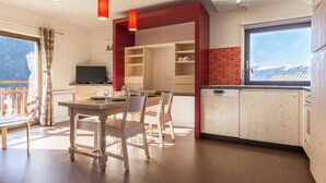 Una cocina moderna con armarios de madera, un comedor con mesa y sillas, y un amplio ventanal con vistas a montañas nevadas.