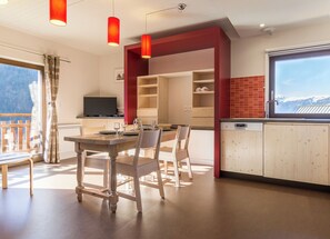 Una cocina moderna con armarios de madera, un comedor con mesa y sillas, y un amplio ventanal con vistas a montañas nevadas.