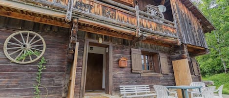 A rustic wooden building with a balcony, a wooden wheel, and outdoor seating.