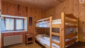 A wooden cabin room with bunk beds, a small table, a window with curtains, and a radiator. - LE PLANAY - NOTRE DAME DE BELLECOMBE (NOTRE DAME DE BELLECOMBE)