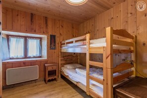 Een houten kamer met stapelbedden, een klein tafeltje, een raam met gordijnen en een radiator.