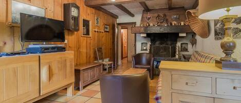 Un interior rústico con paredes de madera, chimenea, televisor y comedor.
