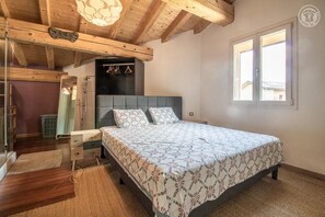 Une chambre à coucher avec un lit, des poutres en bois au plafond, une fenêtre et un luminaire suspendu.