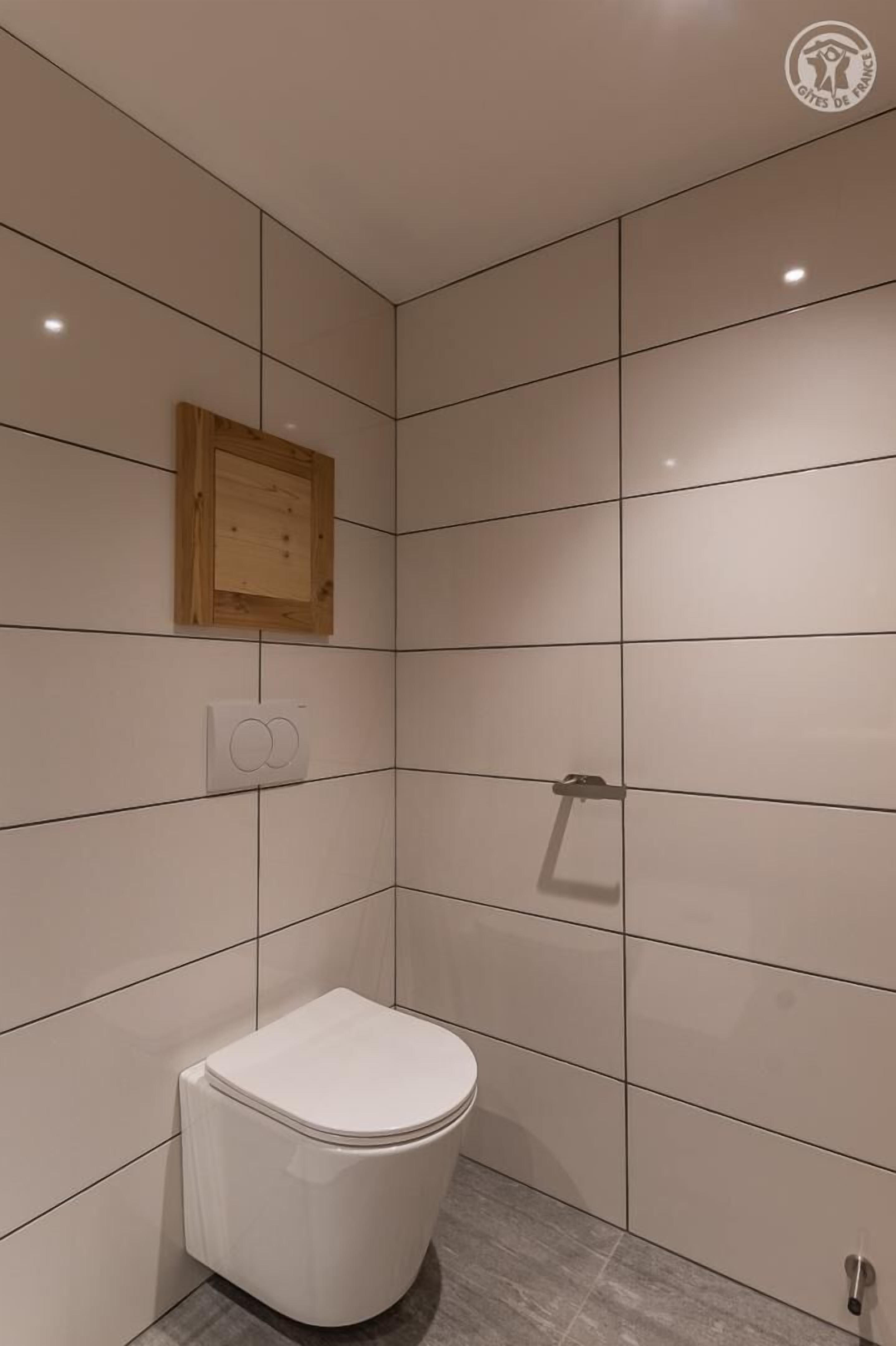 Une petite salle de bain moderne avec des carreaux blancs, des toilettes blanches, un panneau en bois au-dessus des toilettes et un porte-serviettes.
