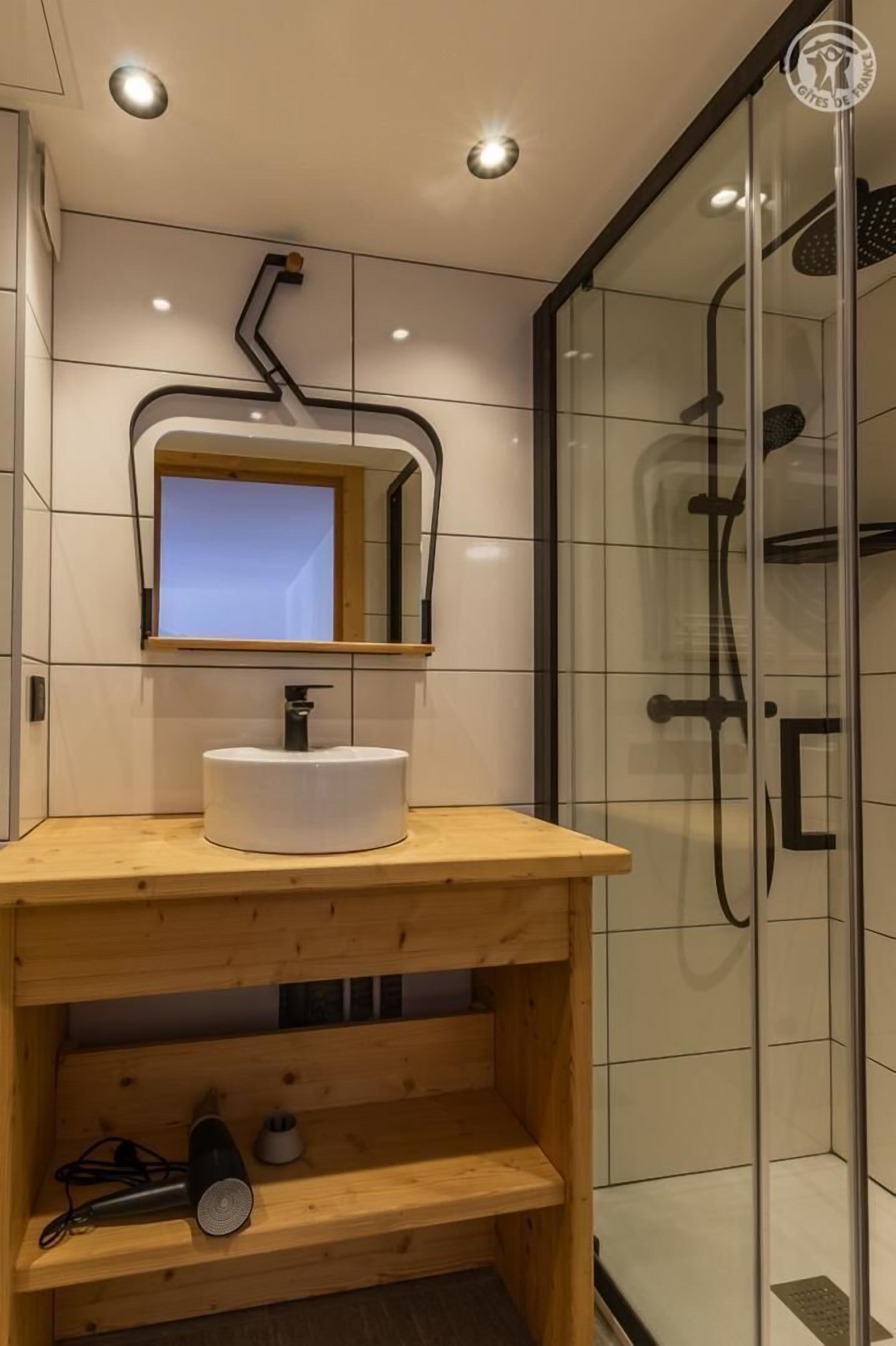 Une salle de bain avec un lavabo blanc, un meuble-lavabo en bois et une cabine de douche en verre.
