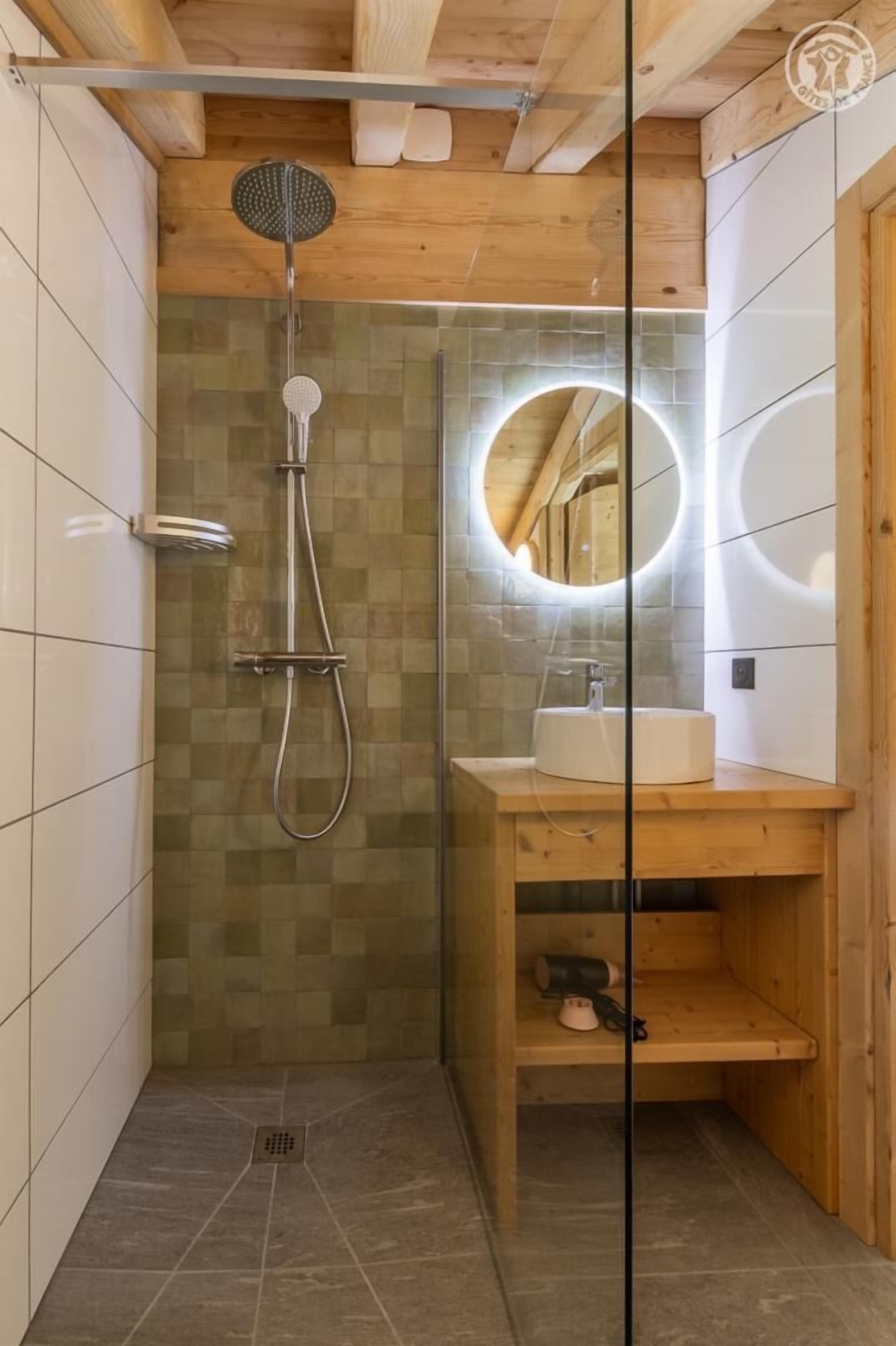 Een douche met een glazen deur, een houten plafond en een betegelde wand.