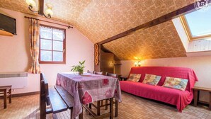 Une pièce chaleureuse avec une table à manger, des chaises, un canapé rouge et une petite fenêtre.