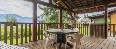 A wooden deck with a table and chairs, overlooking a mountainous landscape.