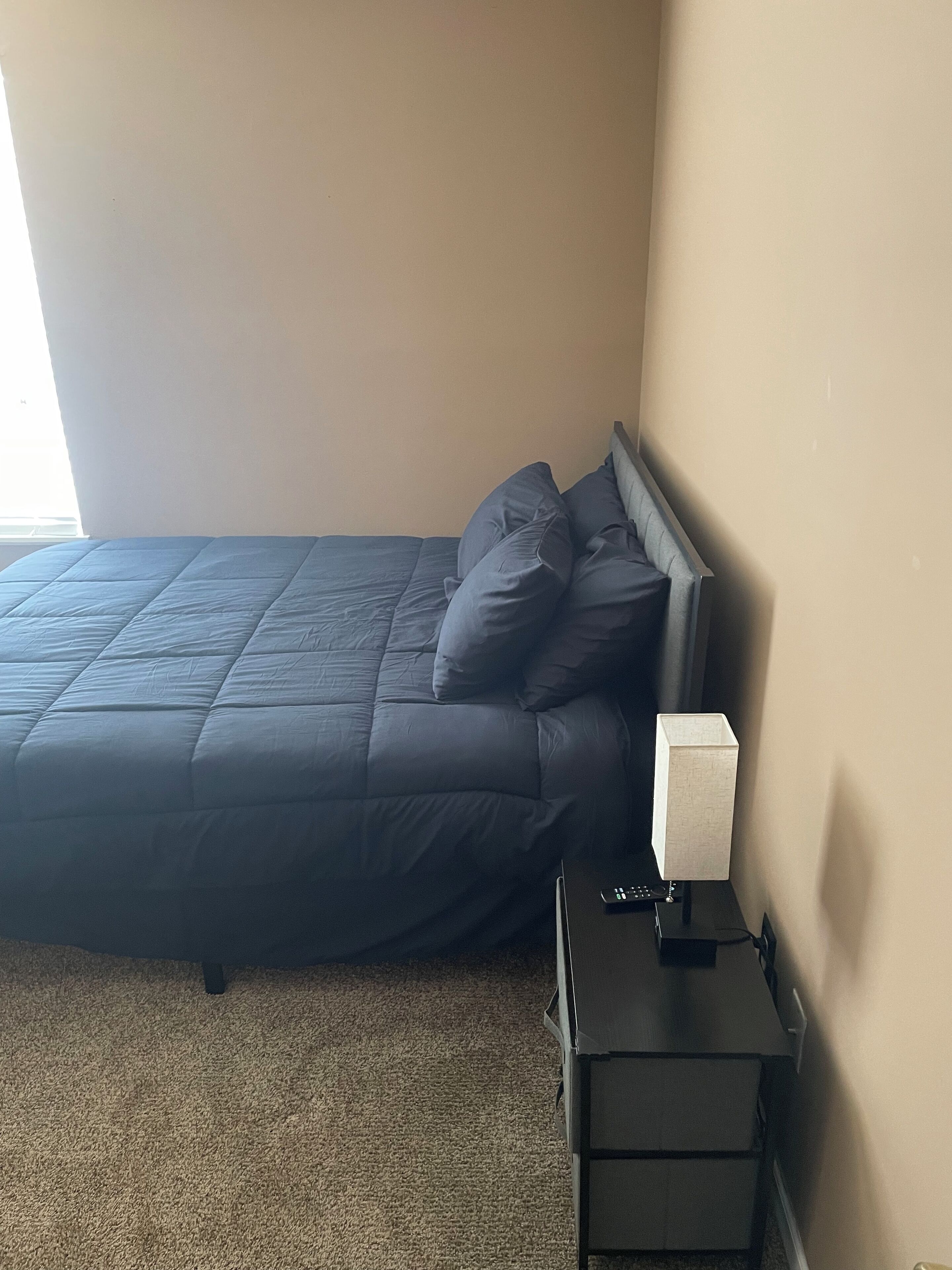 Ein Schlafzimmer mit einem Bett, Kissen, einem Nachttisch mit Lampe und Teppichboden.
