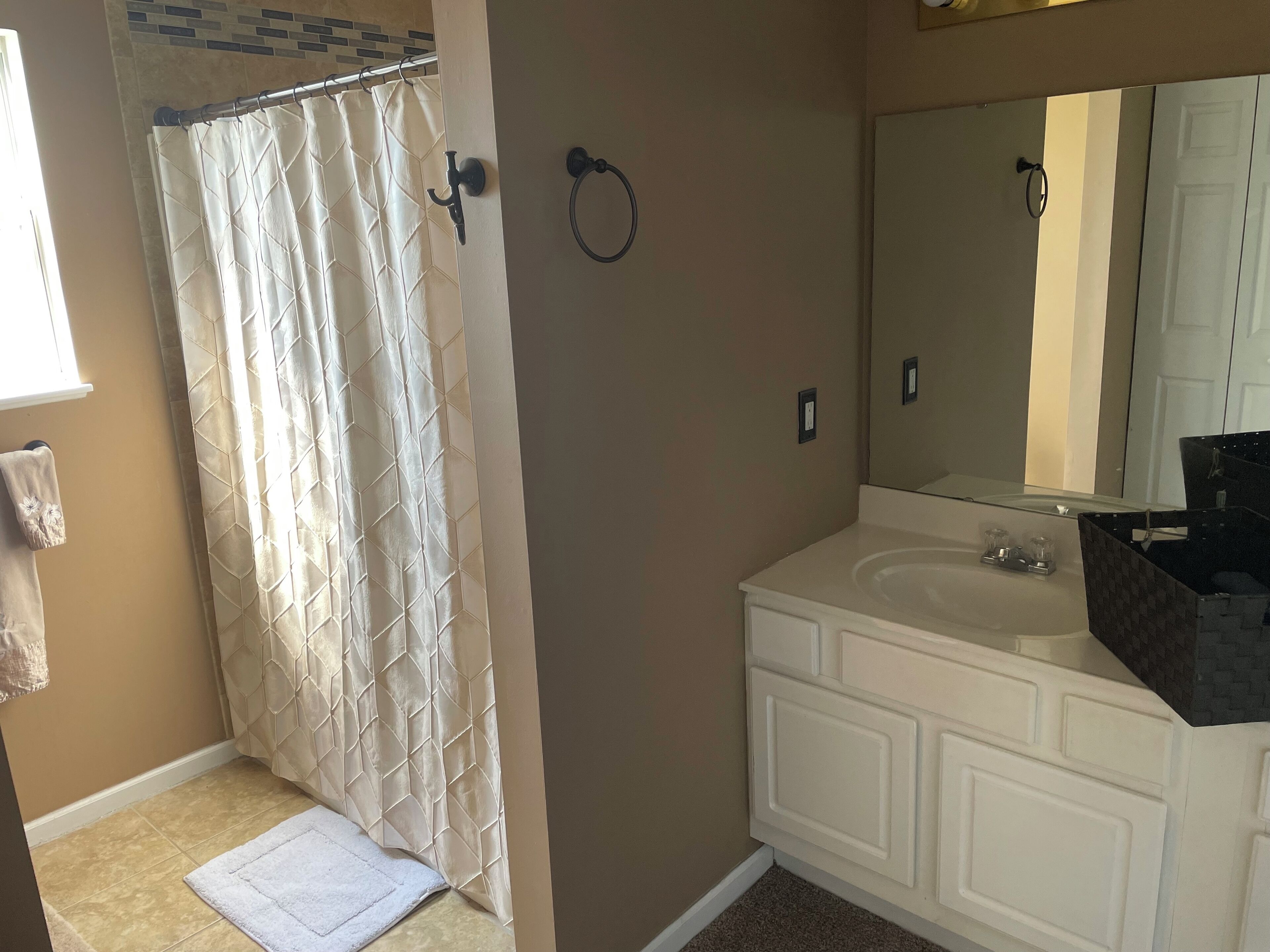 Une salle de bain avec un rideau de douche, un porte-serviettes, un lavabo et un miroir.