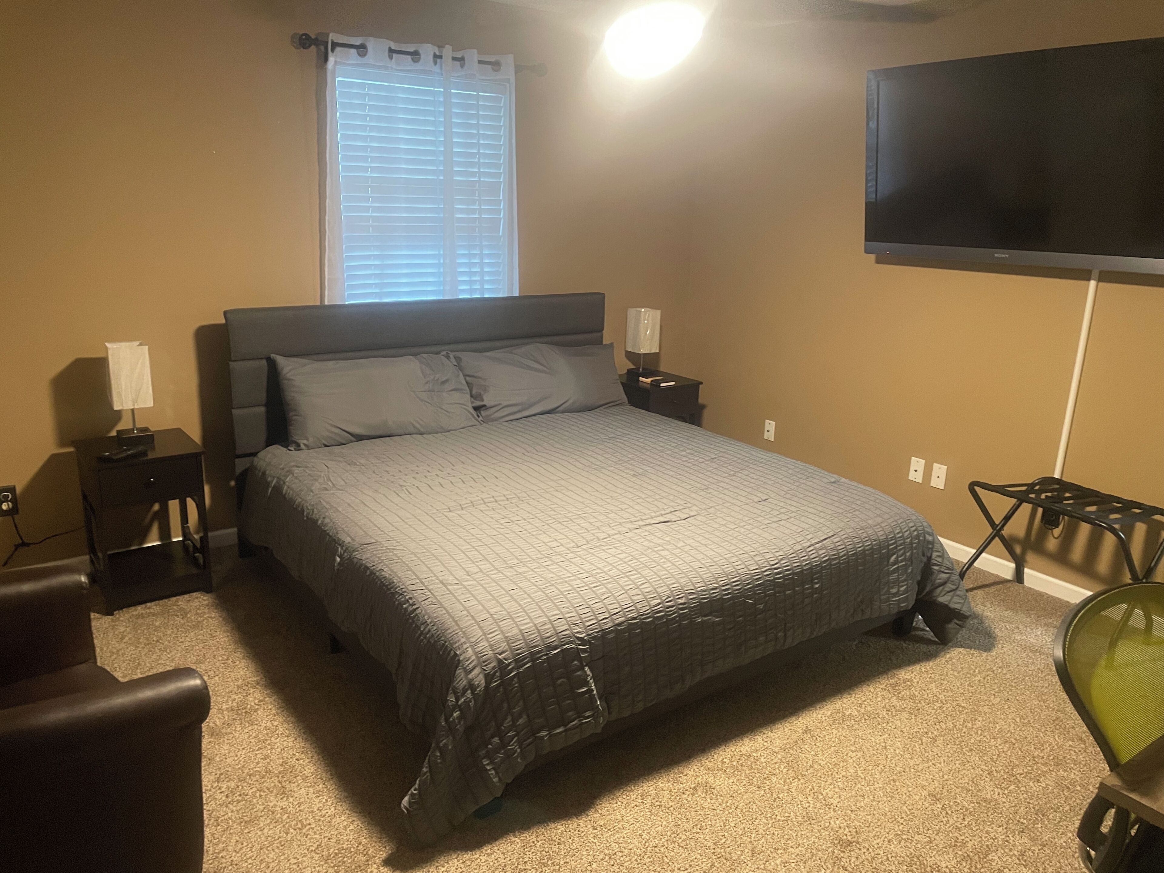Un dormitorio con cama, mesitas de noche, televisor y una silla.