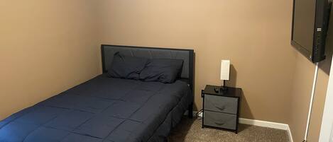 Un dormitorio con cama, mesita de noche, televisor y una frase motivadora en la pared.