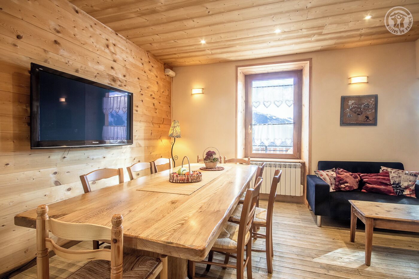 Un intérieur en bois comprenant une table à manger, des chaises, un téléviseur, une fenêtre donnant sur un beau paysage et un canapé.