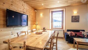 Un intérieur en bois comprenant une table à manger, des chaises, un téléviseur, une fenêtre donnant sur un beau paysage et un canapé.