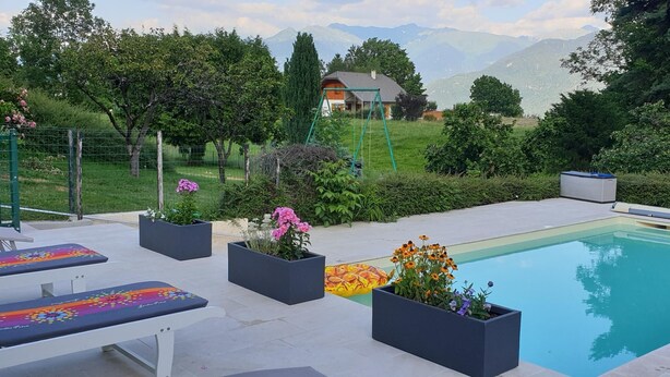 A swimming pool with lounge chairs, flower planters, and a grassy area with a house and mountains in the background. - LA PLANTAZ - CLERY - Gîte (CLERY)