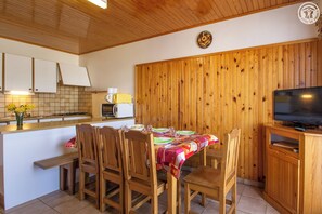 Uma cozinha acolhedora com armários de madeira, uma mesa de jantar posta para quatro pessoas e uma televisão sobre um suporte de madeira.