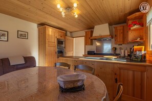 A wooden interior with a dining table, chairs, a kitchen area with wooden cabinets, a microwave, and a stove. - LE CREY - CREST VOLAND COHENNOZ (CREST VOLAND COHENNOZ)
