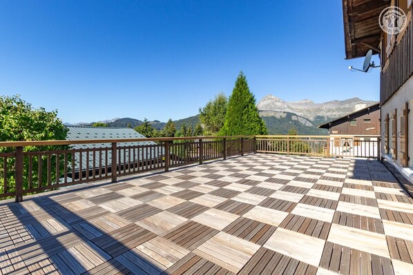 A checkered wooden deck with a wooden railing, overlooking a mountainous landscape.