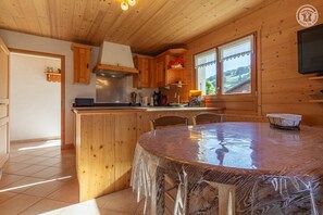 A wooden cabin interior with a kitchen, dining area, and a TV mounted on the wall.