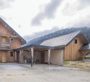 A rustic barn with a covered area, wooden exterior, and a mountainous backdrop.