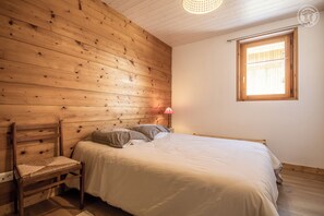 Ein Zimmer mit Holzwänden, einem Bett, einem Sessel, einem Nachttisch und einem Fenster.