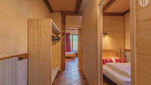 A wooden interior with a bed, a radiator, and a view into another room.