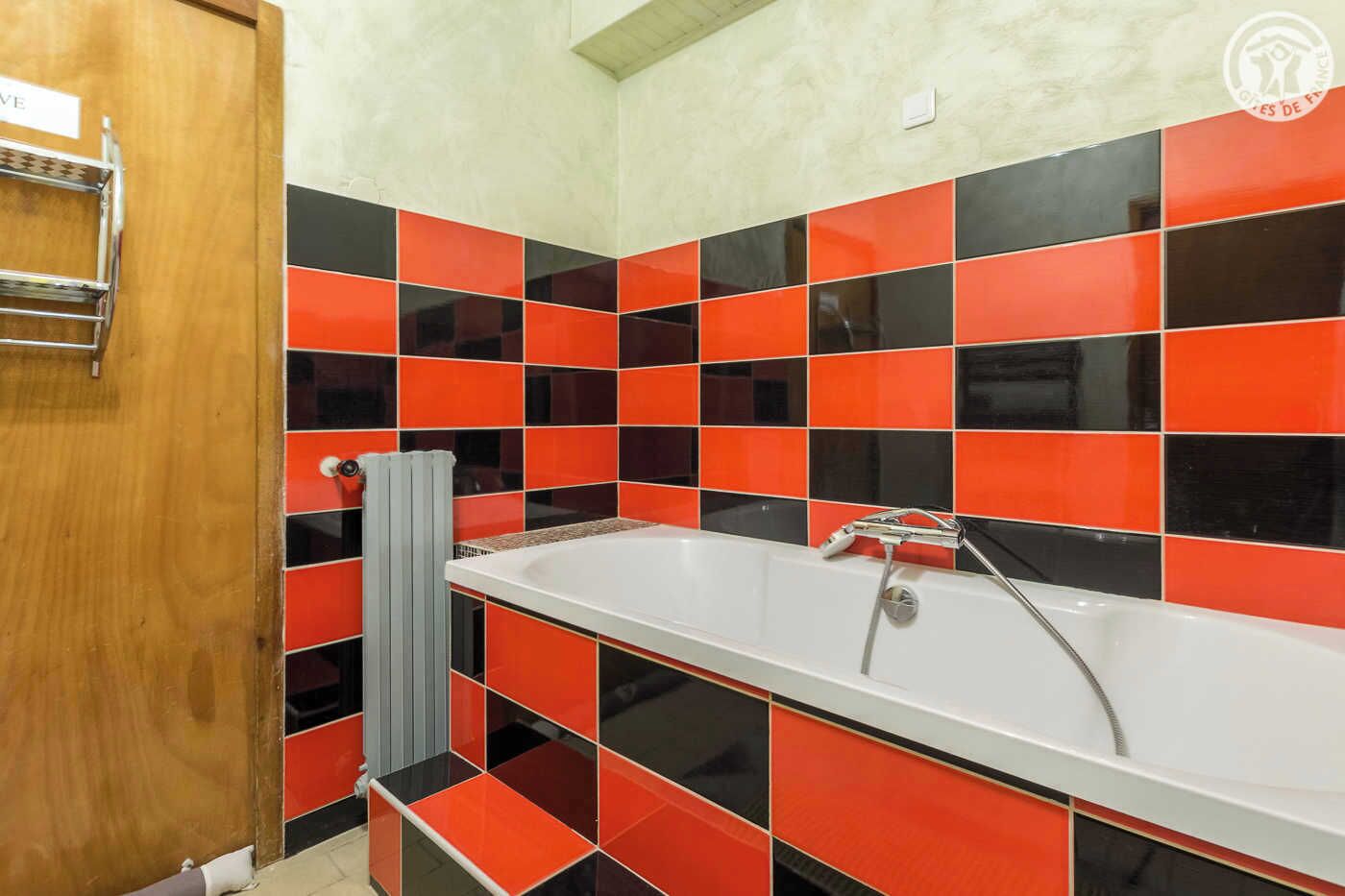 Une salle de bain avec une baignoire blanche, des carreaux rouges et noirs, un porte-serviettes et un radiateur.
