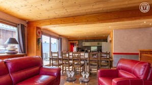 A cozy living room with red leather sofas, a wooden coffee table, and a dining area with wooden chairs and a central table.