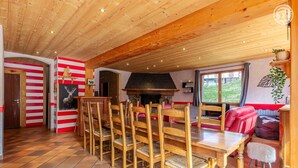 A dining area with wooden chairs and a long table, a fireplace, and a red and white striped wall.