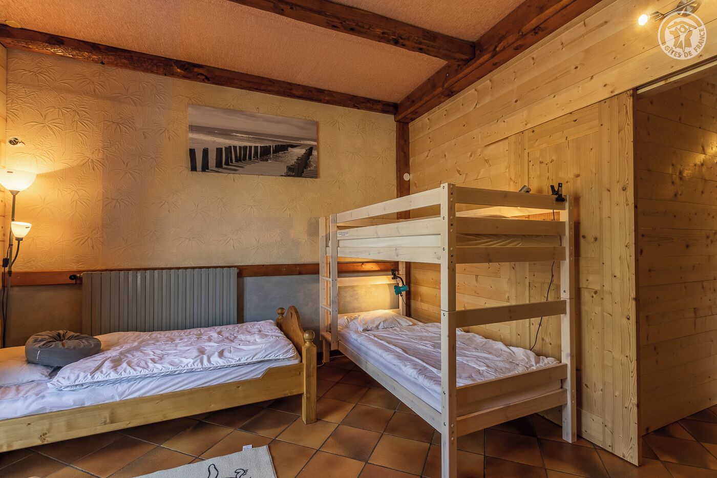 Ein Zimmer mit zwei Etagenbetten, einem Heizkörper, einer Wandleuchte und einem gerahmten Bild.