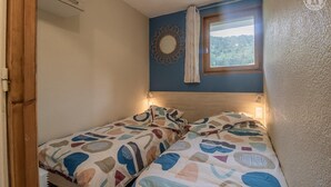 Un dormitorio pequeño con dos camas, una ventana con vistas al exterior y un espejo decorativo en la pared.
