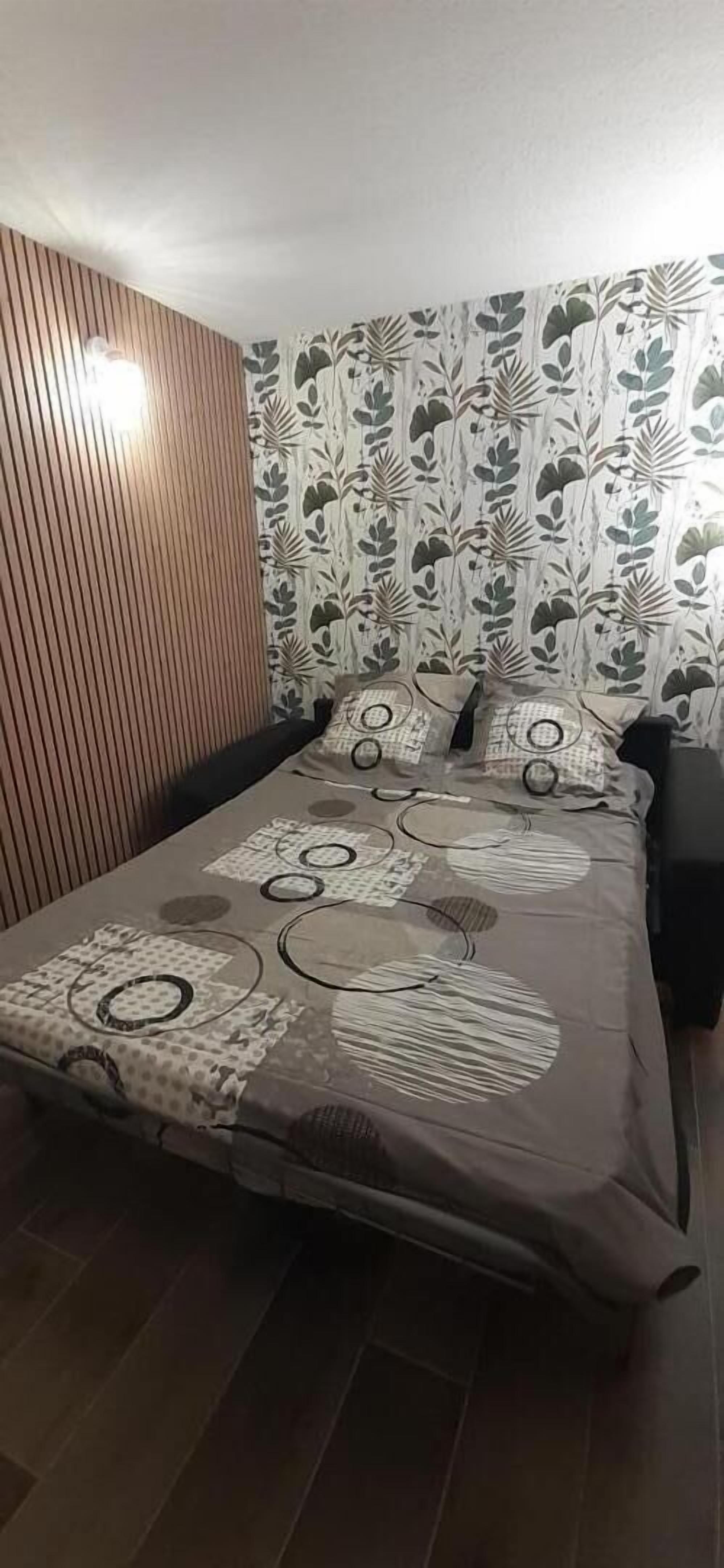 A bedroom with a bed, a wooden slat wall, and patterned wallpaper.