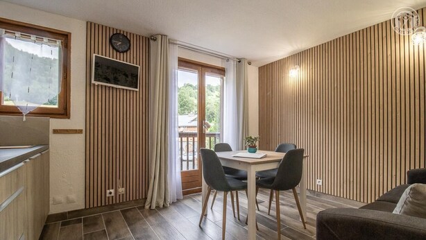 Una cocina moderna con armarios de madera, un comedor con mesa y sillas, y vistas a través de una ventana.