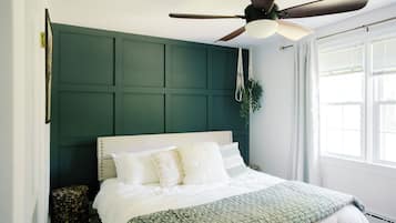 A bedroom with a bed, a ceiling fan, a window with blinds, and a green wall panel.
