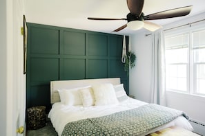 Ein Schlafzimmer mit einem Bett, einem Deckenventilator, einem Fenster mit Jalousien und einer grünen Wandverkleidung.