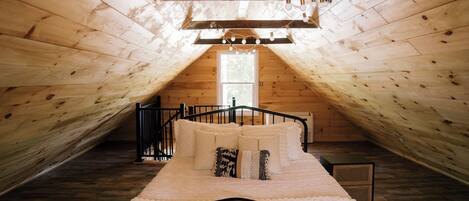 Un dormitorio acogedor en el ático, con techo inclinado, cama con cabecera y ventana que proporciona luz natural.
