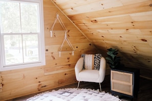 Ein gemütliches Zimmer mit Holzwänden, einem weißen Stuhl, einem Rattan-Schrank und einem Wandbehang aus Makramee.