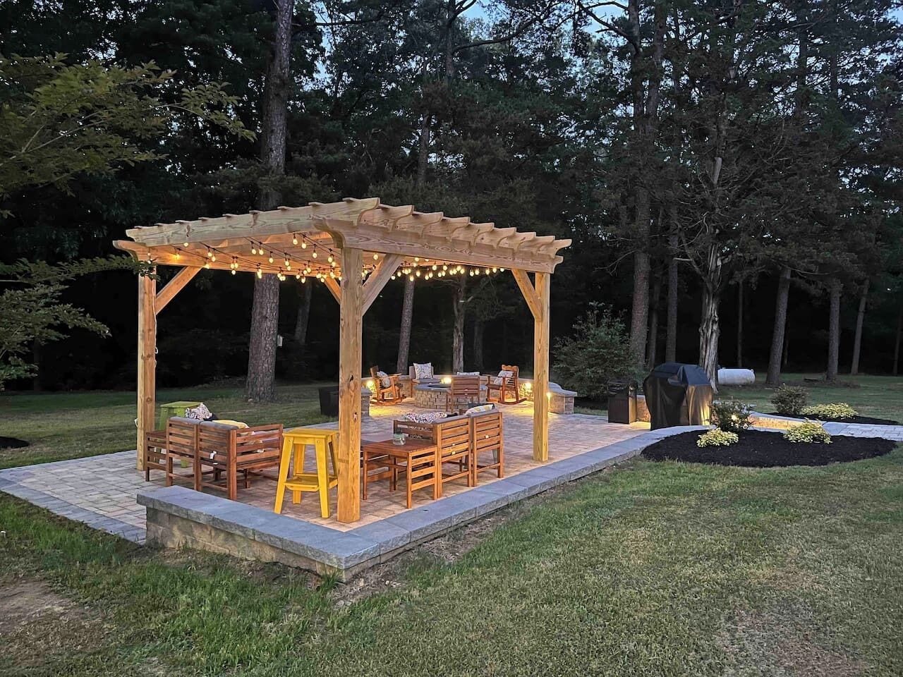 Una pergola in legno con luci a tenda, mobili da esterno e un giardino curato.