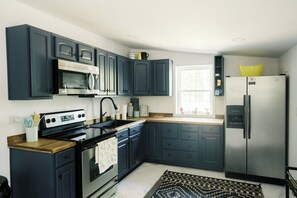 Une cuisine moderne avec des meubles de couleur bleu foncé, des appareils en acier inoxydable et une fenêtre laissant entrer la lumière naturelle.