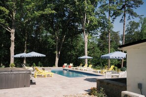 Une piscine entourée d’arbres, avec des chaises longues et des parasols.