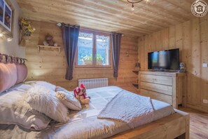 Ein gemütliches Schlafzimmer einer Holzblockhütte mit einem Bett, einem Fernseher und einem Fenster mit Vorhängen.