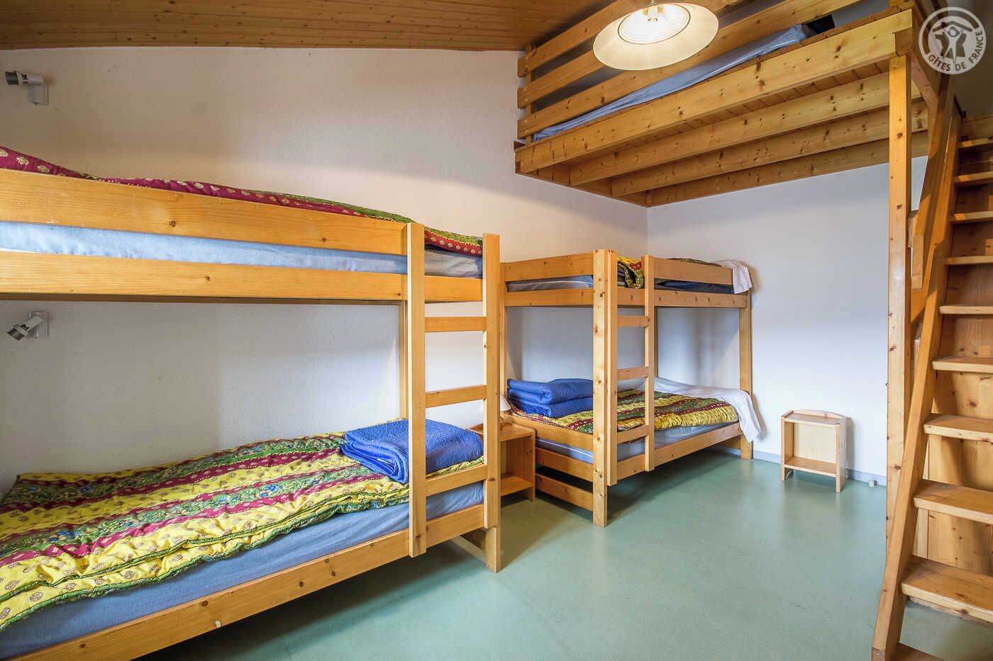 A dormitory room with bunk beds, a small wooden stool, and a wooden ladder.