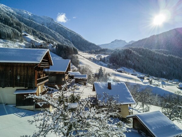 A snow-covered village with wooden buildings, a clear sky, and a mountain backdrop.