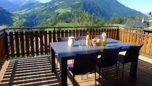A wooden deck with a table set for two, overlooking a mountainous landscape.