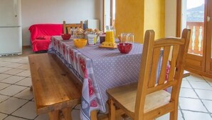 Ein Essbereich mit einem Holztisch, gedeckt für zwei Personen, einer Bank und einem roten Stuhl.
