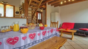 Ein gemütlicher Essbereich mit einem Holztisch, gedeckt für eine Mahlzeit, einer Treppe und einem Wohnzimmer mit einer Couch und einer roten Decke.